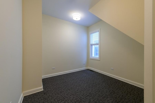 additional living space with dark colored carpet and baseboards