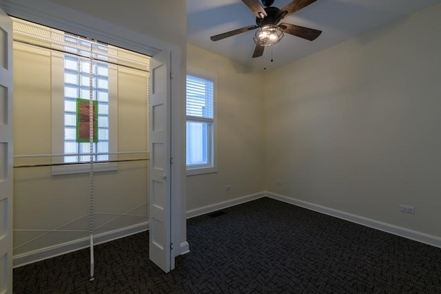 spare room with a ceiling fan, dark carpet, and baseboards