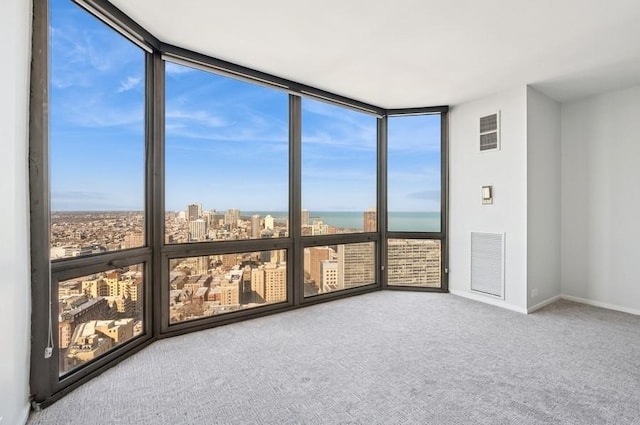 carpeted spare room with a wall of windows, visible vents, a city view, and baseboards