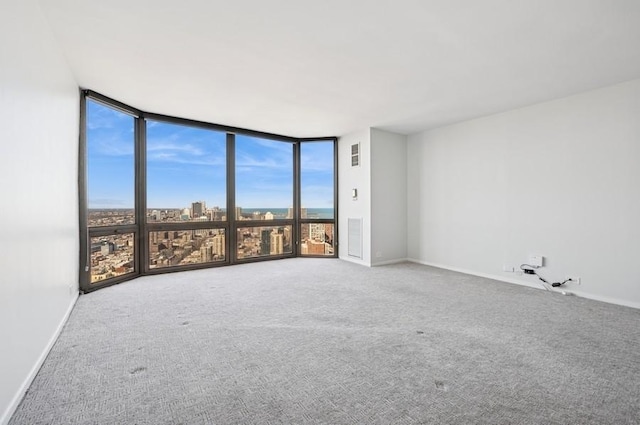 carpeted empty room featuring baseboards, a city view, and floor to ceiling windows