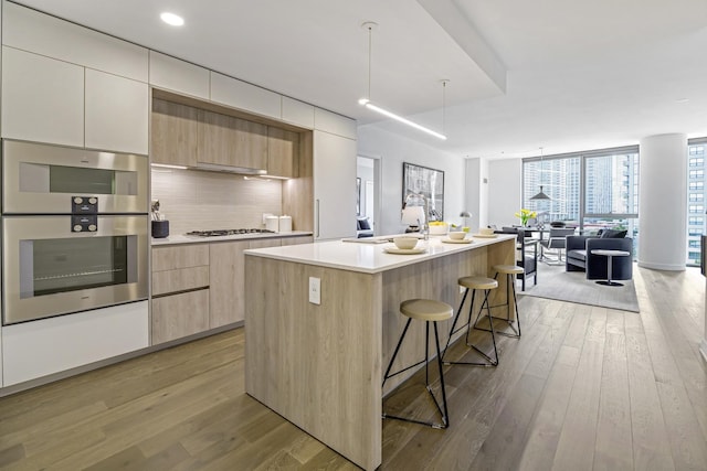 kitchen featuring light wood-style flooring, stainless steel appliances, expansive windows, tasteful backsplash, and modern cabinets