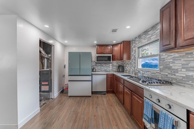 kitchen featuring appliances with stainless steel finishes, backsplash, light wood-type flooring, and a sink