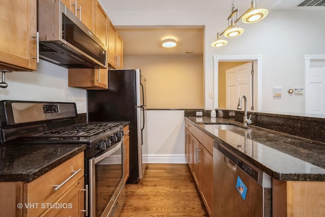 kitchen with light wood finished floors, stainless steel appliances, brown cabinetry, and a sink