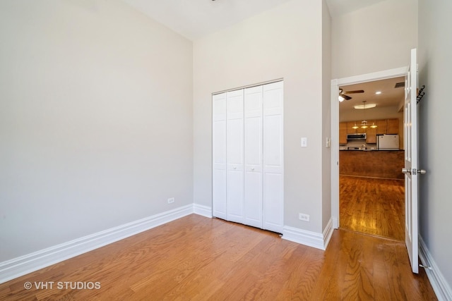 unfurnished bedroom featuring fridge, wood finished floors, baseboards, and a closet