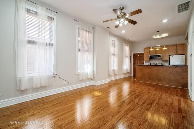 unfurnished living room featuring a wealth of natural light, visible vents, light wood-style floors, and a ceiling fan