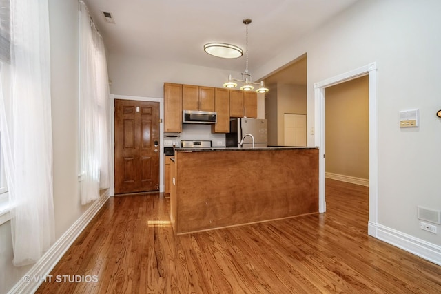 kitchen with dark countertops, visible vents, decorative light fixtures, appliances with stainless steel finishes, and wood finished floors