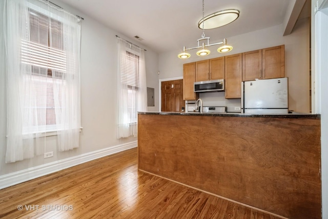 kitchen with dark countertops, stainless steel microwave, brown cabinets, freestanding refrigerator, and wood finished floors