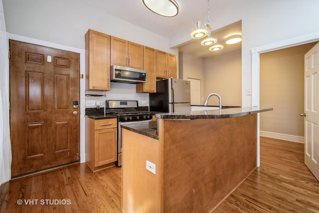 kitchen with pendant lighting, wood finished floors, stainless steel appliances, dark stone counters, and brown cabinetry