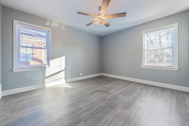 empty room featuring ceiling fan, wood finished floors, a wealth of natural light, and baseboards