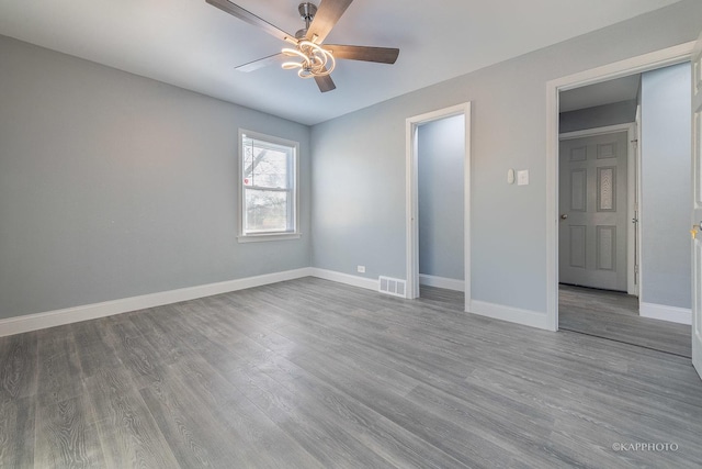 unfurnished bedroom featuring a ceiling fan, visible vents, baseboards, and wood finished floors