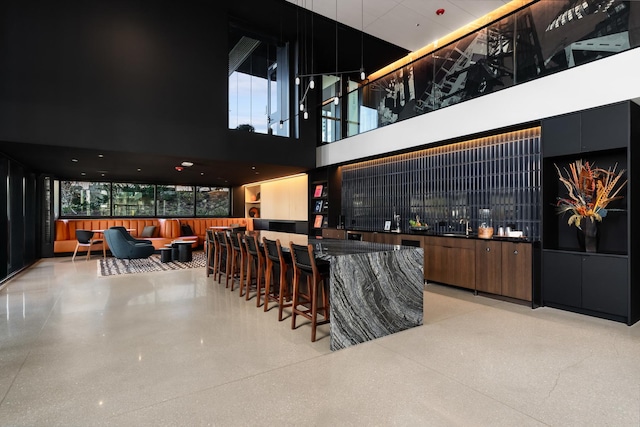 bar with light speckled floor, a towering ceiling, and wet bar