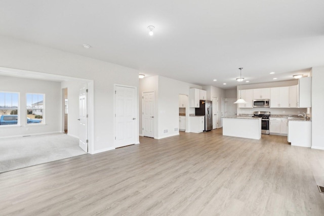 unfurnished living room with light wood-type flooring, a sink, baseboards, and recessed lighting