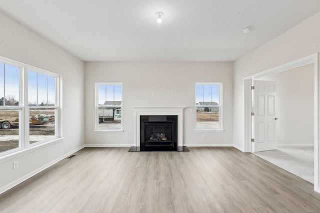 unfurnished living room featuring visible vents, baseboards, wood finished floors, and a glass covered fireplace