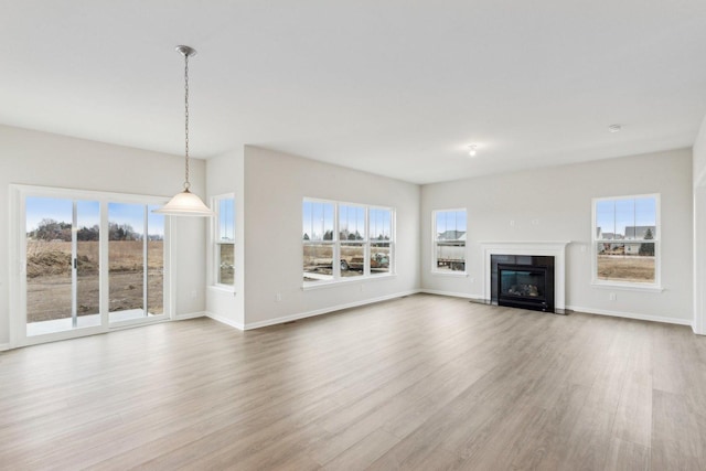 unfurnished living room featuring a glass covered fireplace, wood finished floors, a wealth of natural light, and baseboards