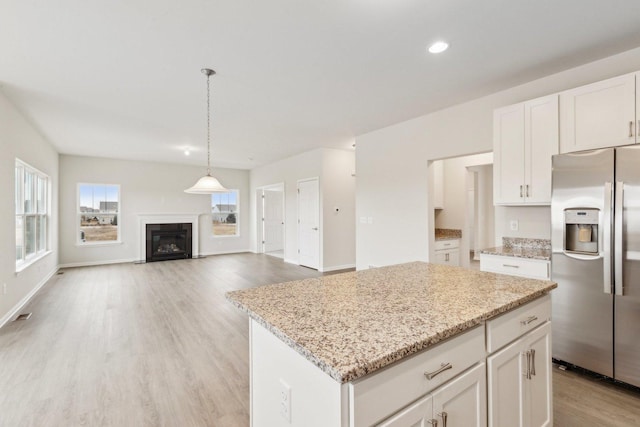 kitchen featuring stainless steel fridge with ice dispenser, light stone counters, light wood-type flooring, a fireplace, and white cabinetry