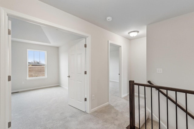 hallway featuring carpet, baseboards, and an upstairs landing