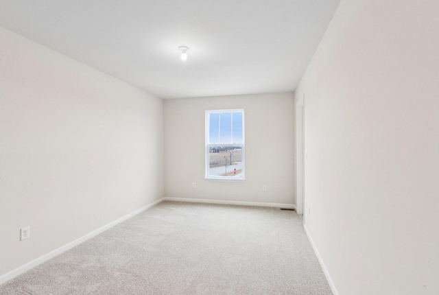 spare room with baseboards and light colored carpet