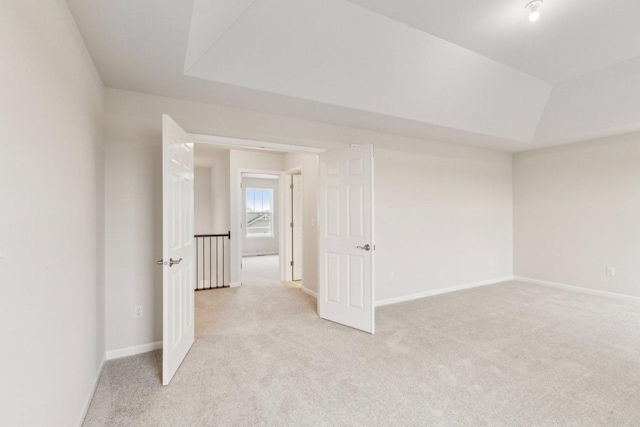 empty room with a tray ceiling, light carpet, and baseboards