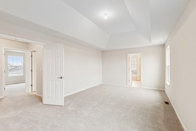 unfurnished room with a tray ceiling, carpet flooring, visible vents, and baseboards