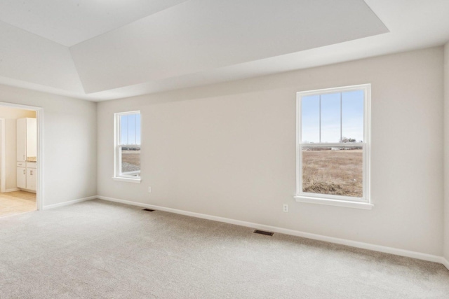 empty room with carpet floors, a raised ceiling, visible vents, and baseboards