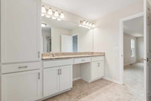 bathroom with baseboards, double vanity, a sink, and a shower stall