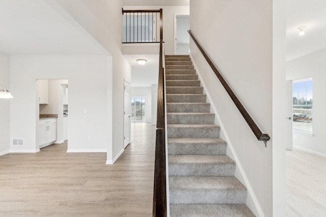 stairway with visible vents, a towering ceiling, baseboards, and wood finished floors