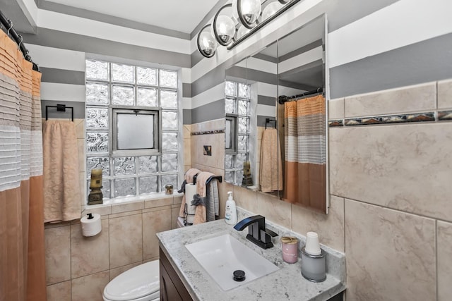 full bath with toilet, tile walls, and vanity