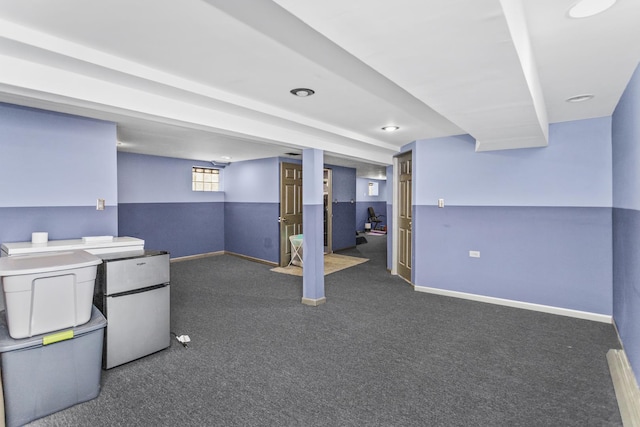 basement with freestanding refrigerator, dark carpet, and baseboards