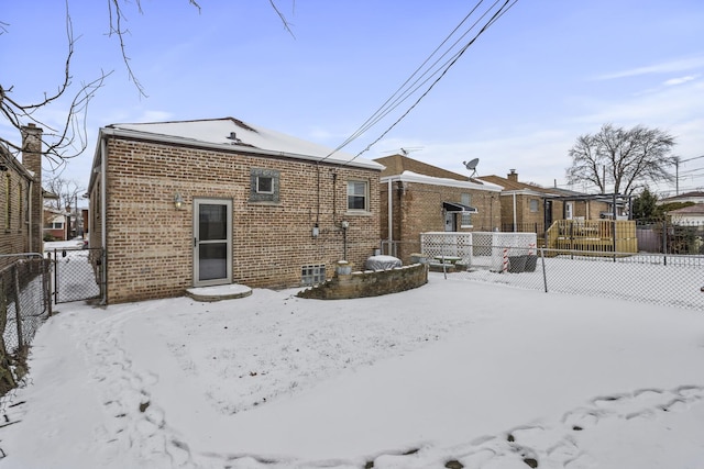 snow covered rear of property featuring fence and brick siding