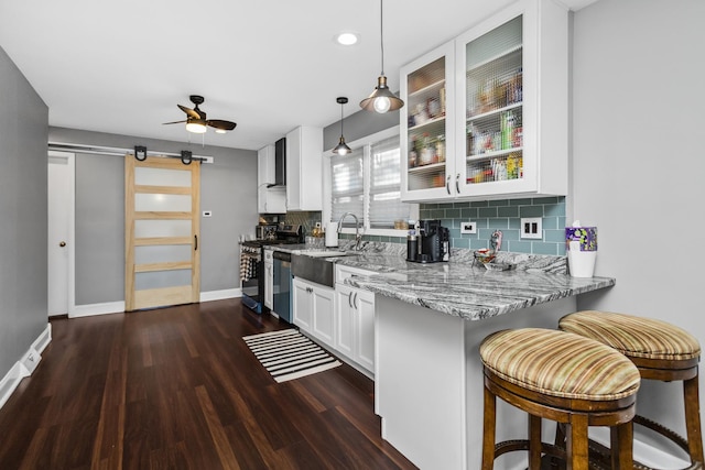 kitchen featuring a barn door, stainless steel appliances, white cabinetry, wall chimney range hood, and glass insert cabinets