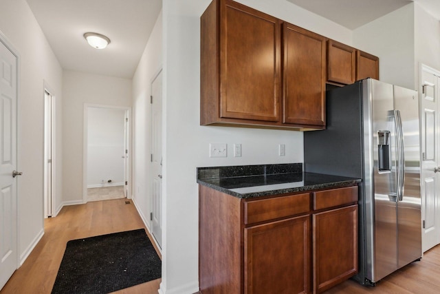 kitchen with light wood-style flooring, baseboards, stainless steel fridge with ice dispenser, dark stone counters, and brown cabinetry