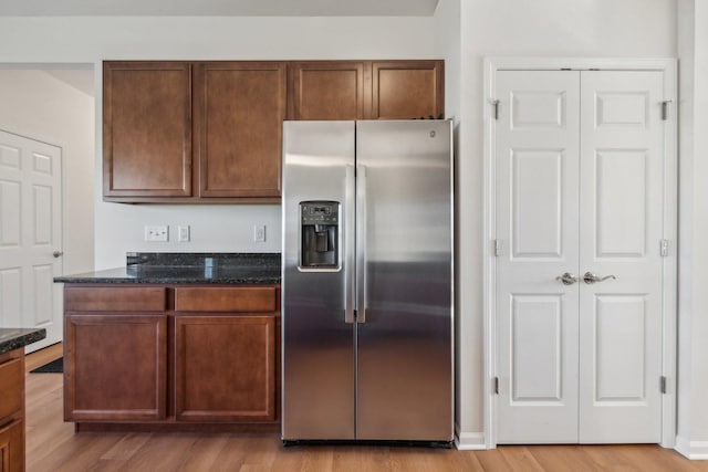 kitchen with light wood-type flooring, dark stone counters, and stainless steel refrigerator with ice dispenser