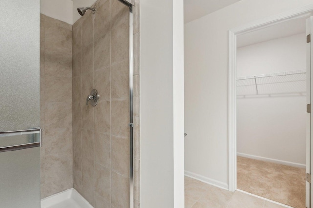 full bath featuring a walk in closet, a shower stall, and baseboards