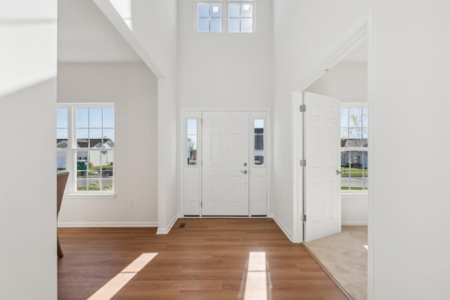 foyer entrance with a towering ceiling, baseboards, and wood finished floors