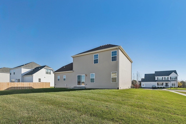 rear view of property featuring a lawn and fence