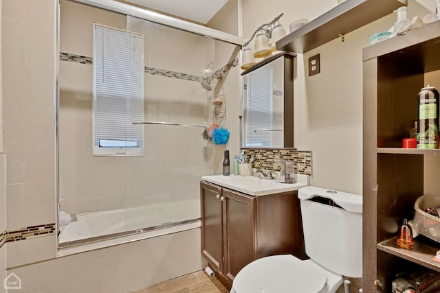 bathroom featuring bath / shower combo with glass door, tasteful backsplash, vanity, and toilet