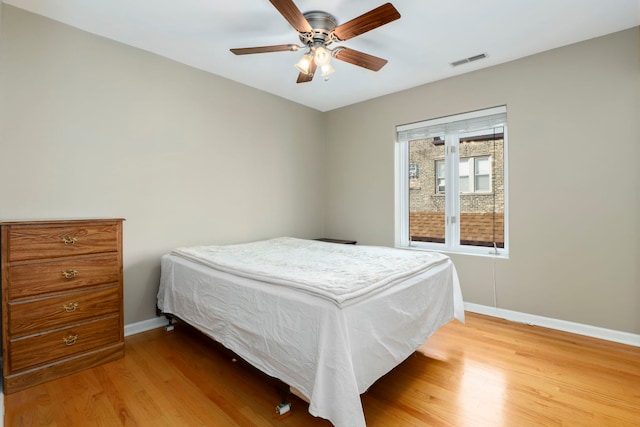 bedroom with visible vents, light wood-style flooring, a ceiling fan, and baseboards