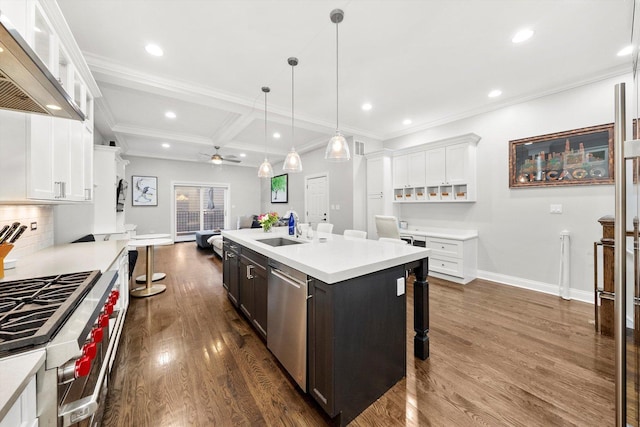 kitchen featuring light countertops, appliances with stainless steel finishes, white cabinetry, a sink, and wall chimney exhaust hood