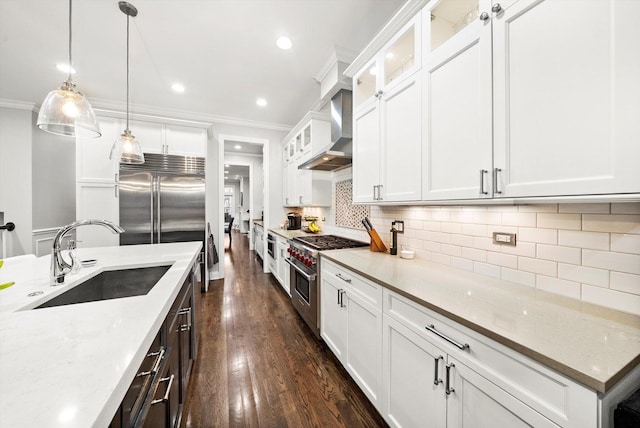 kitchen featuring premium appliances, dark wood-style floors, ornamental molding, a sink, and wall chimney range hood