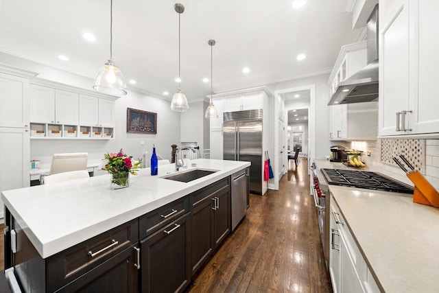 kitchen with high end appliances, white cabinetry, a sink, and wall chimney exhaust hood