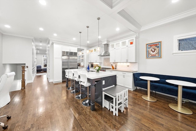 kitchen featuring a breakfast bar, dark wood-style flooring, light countertops, wall chimney range hood, and built in fridge