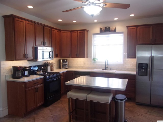 kitchen featuring decorative backsplash, appliances with stainless steel finishes, light countertops, a kitchen bar, and a sink