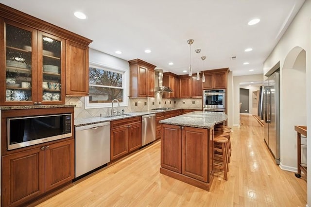 kitchen with light stone counters, a center island, stainless steel appliances, light wood-type flooring, and a sink