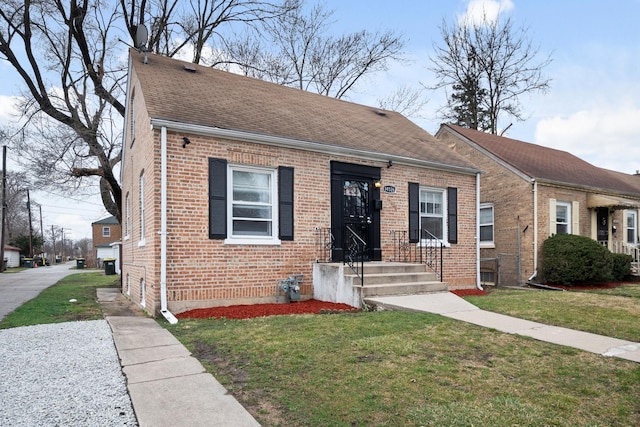 view of front of house with a shingled roof, a front yard, and brick siding