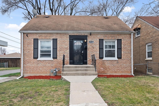 bungalow with brick siding, roof with shingles, a front yard, and fence