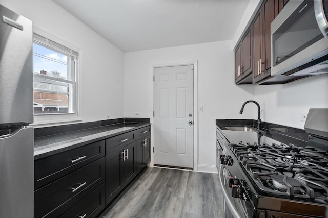 kitchen with stainless steel appliances, light wood-type flooring, a sink, and baseboards