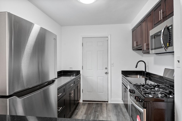 kitchen featuring appliances with stainless steel finishes, dark stone counters, a sink, and wood finished floors