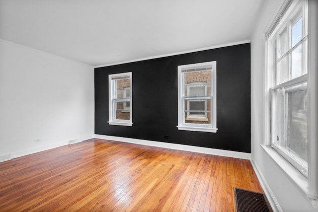 empty room with ornamental molding, visible vents, light wood-style flooring, and baseboards