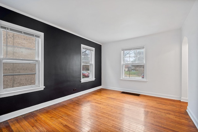 empty room featuring arched walkways, light wood-type flooring, visible vents, and baseboards