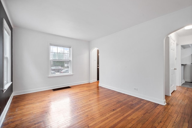 spare room with visible vents, arched walkways, wood-type flooring, and baseboards